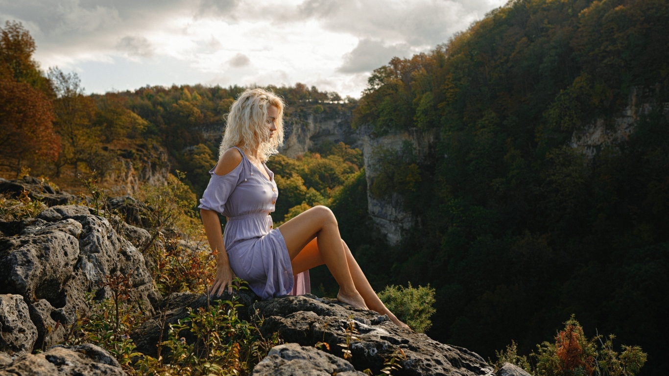 Красивая длинноногая блондинка сидит на краю скалы