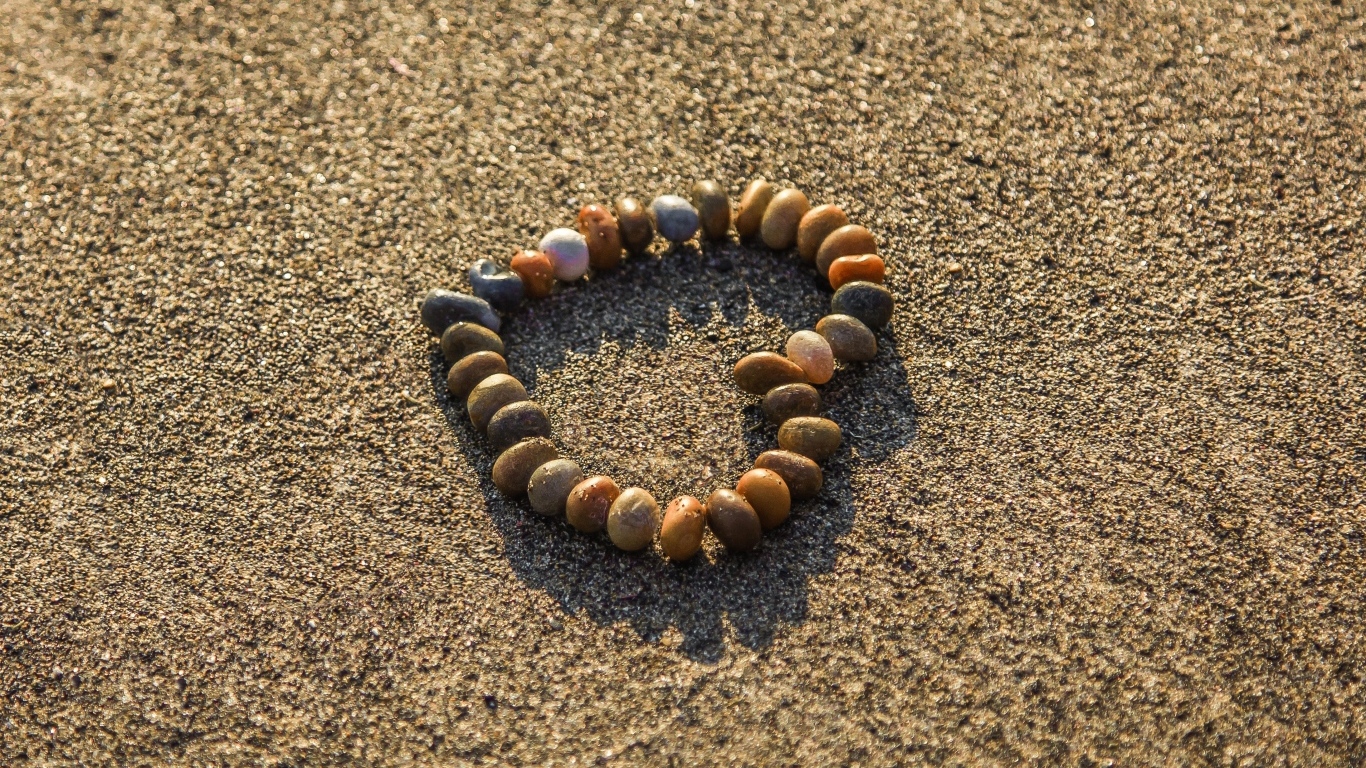 Сердце из камней на морском песке летом