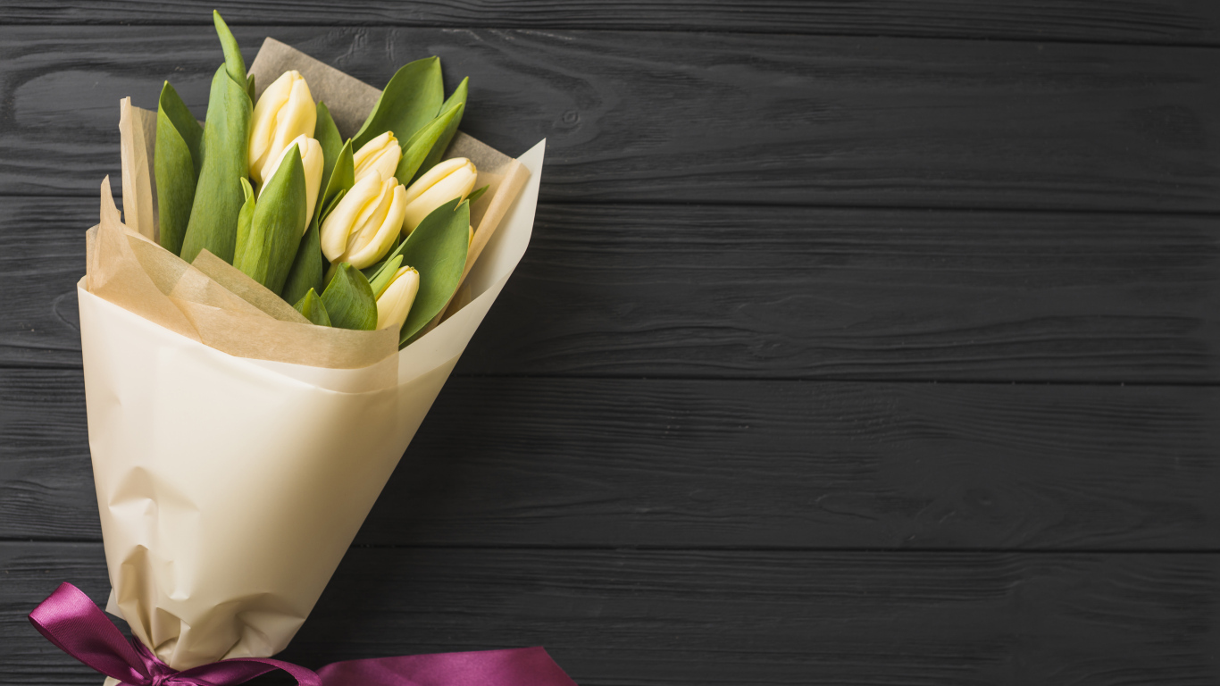 Букет желтых тюльпанов в бумаге на черном столе