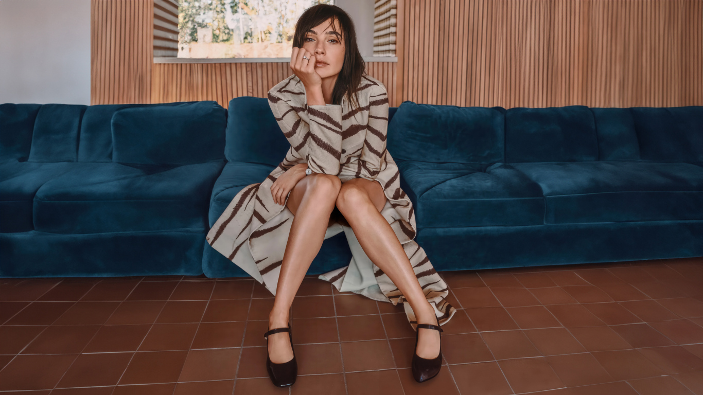 Актриса Галь Гадот в пальто сидит на диване