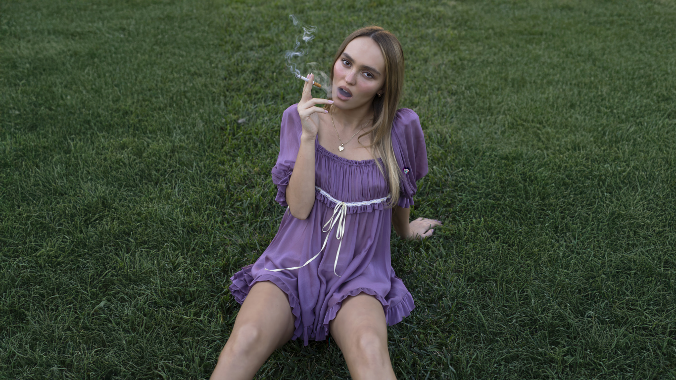 Молодая Лили-Роуз Депп с сигаретой сидит на траве