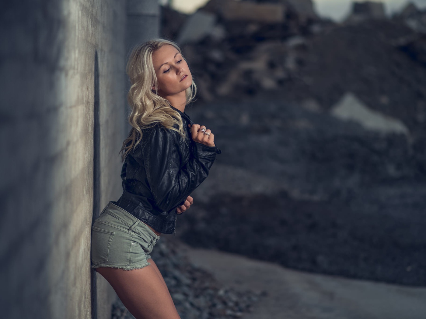 Блондинка в джинсовых шортах стоит у стены