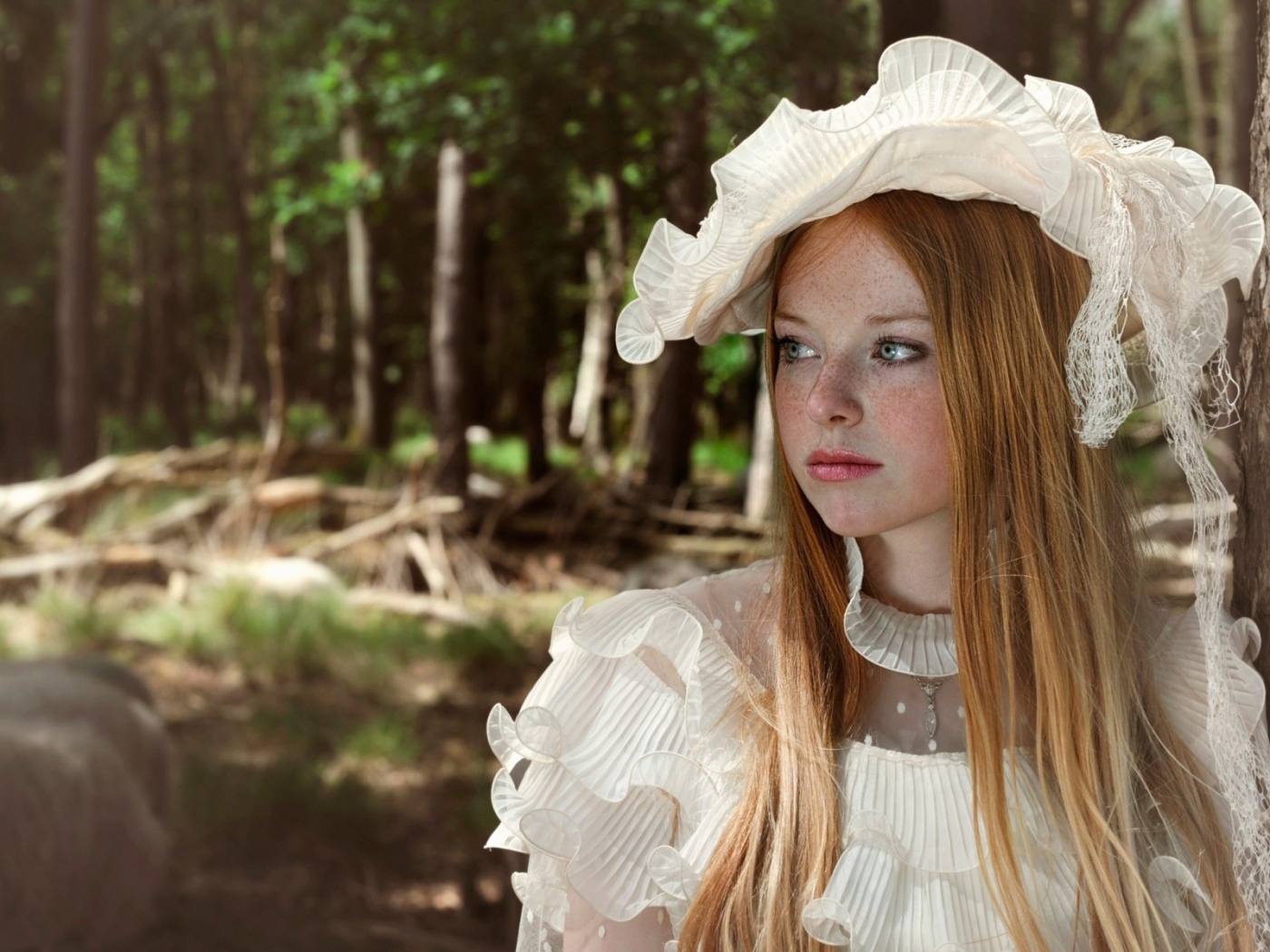 Веснушчатая девушка в белой шляпке стоит у дерева