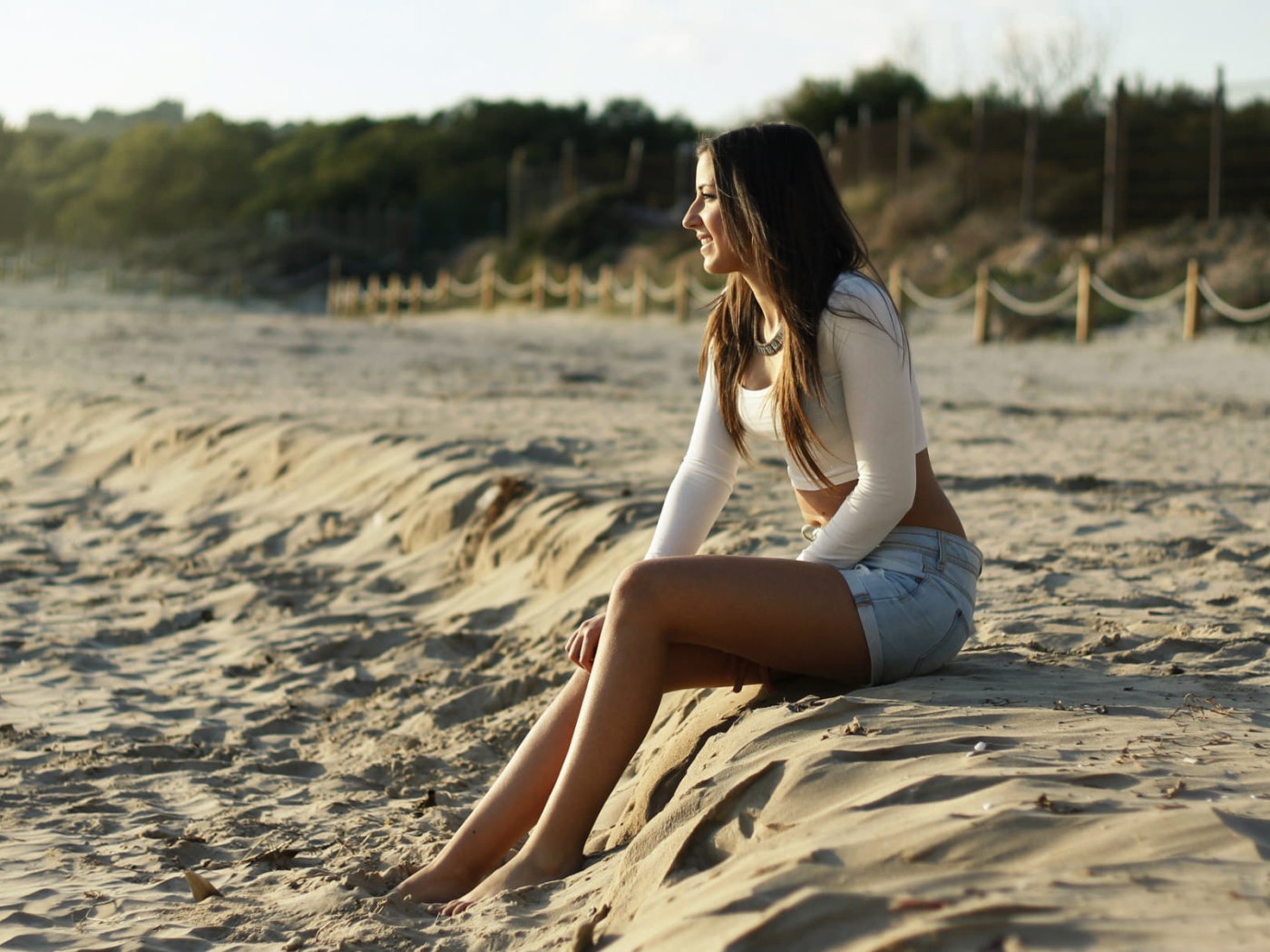 Девушка в джинсовых шортах сидит на песке пляжа