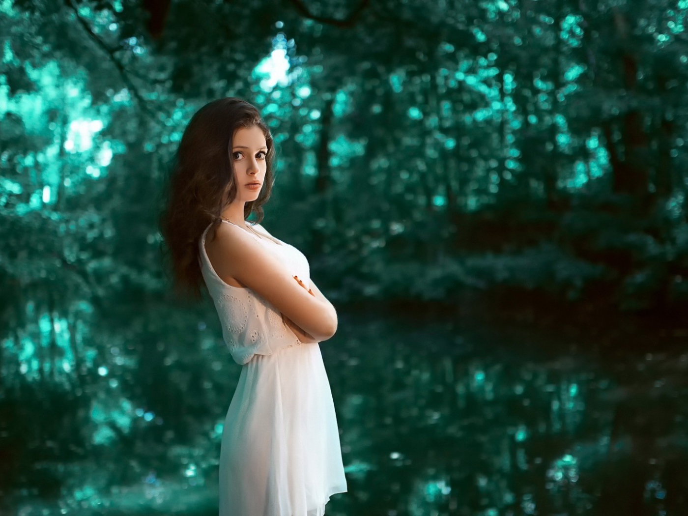 Девушка в белом платье стоит в зеленом лесу