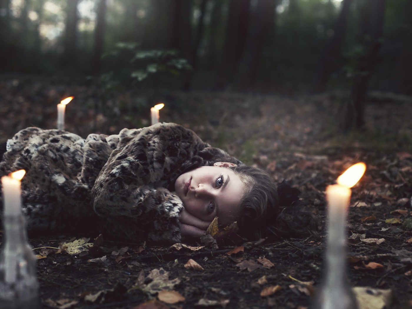 Девушка лежит среди свечей в лесу