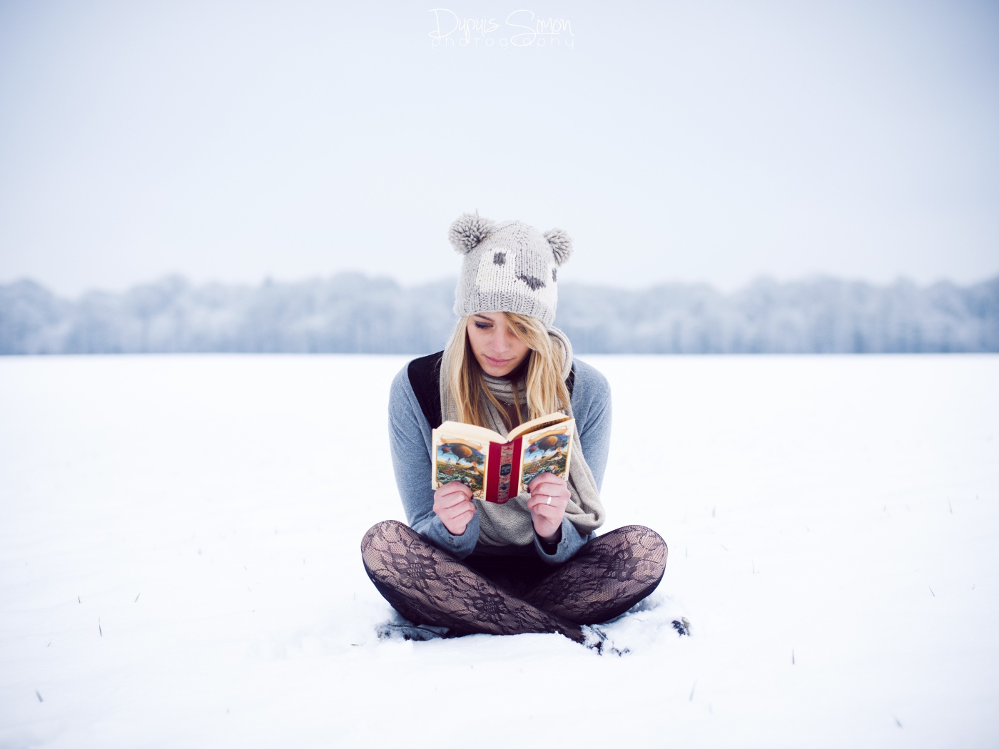 Девушка читает книгу сидя на снегу