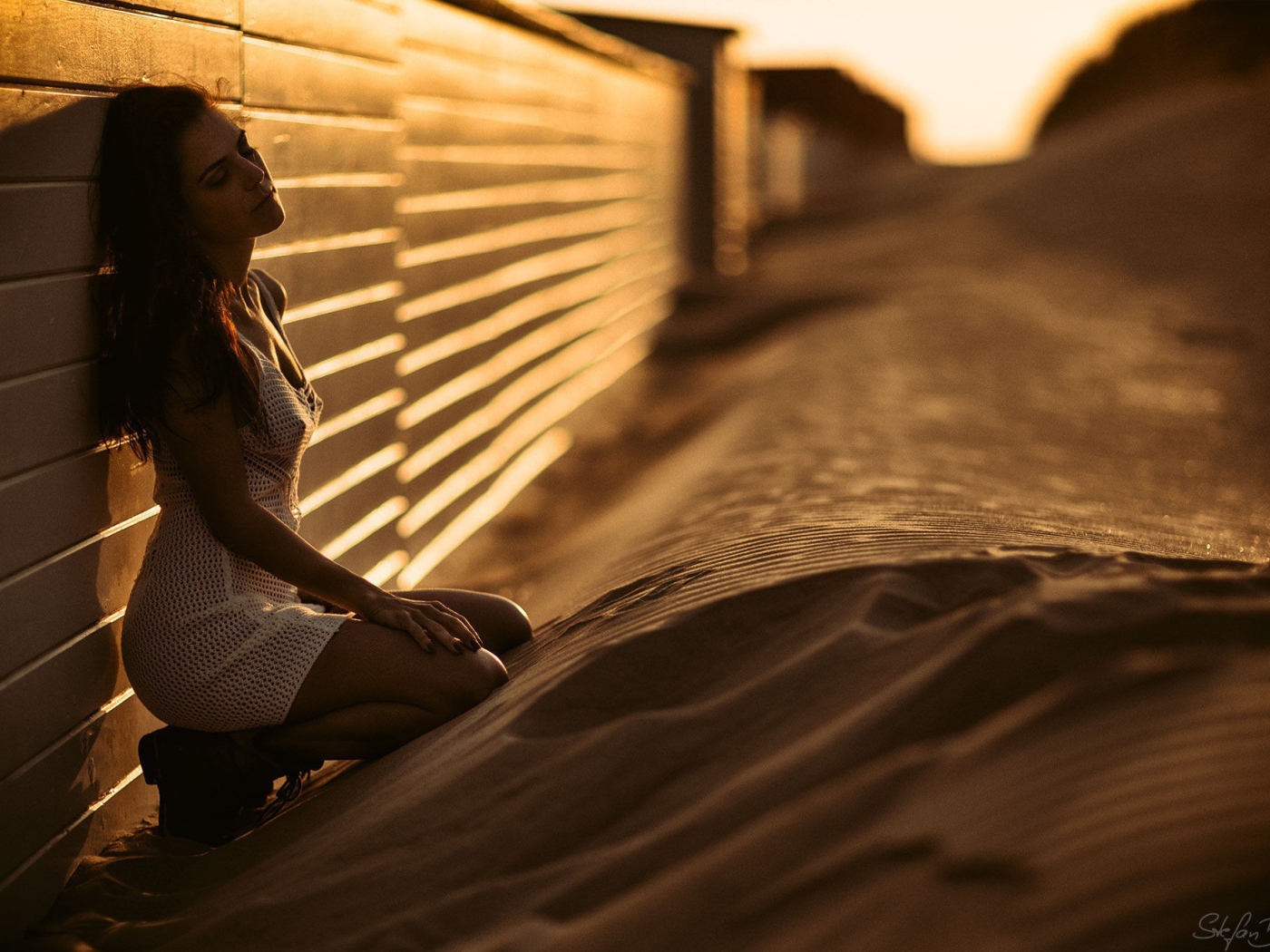 Девушка сидит на песке у забора