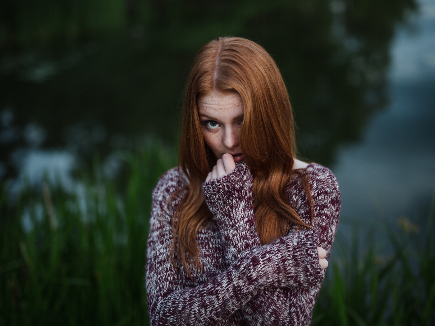 Рыжая девушка в свитере на фоне водоема
