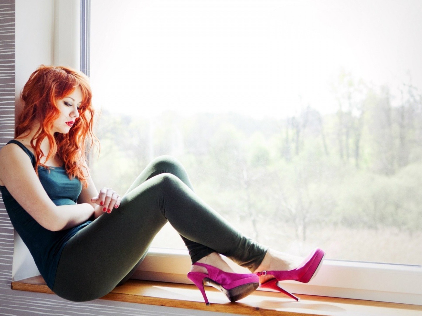 Рыжая девушка в розовых туфлях сидит на окне