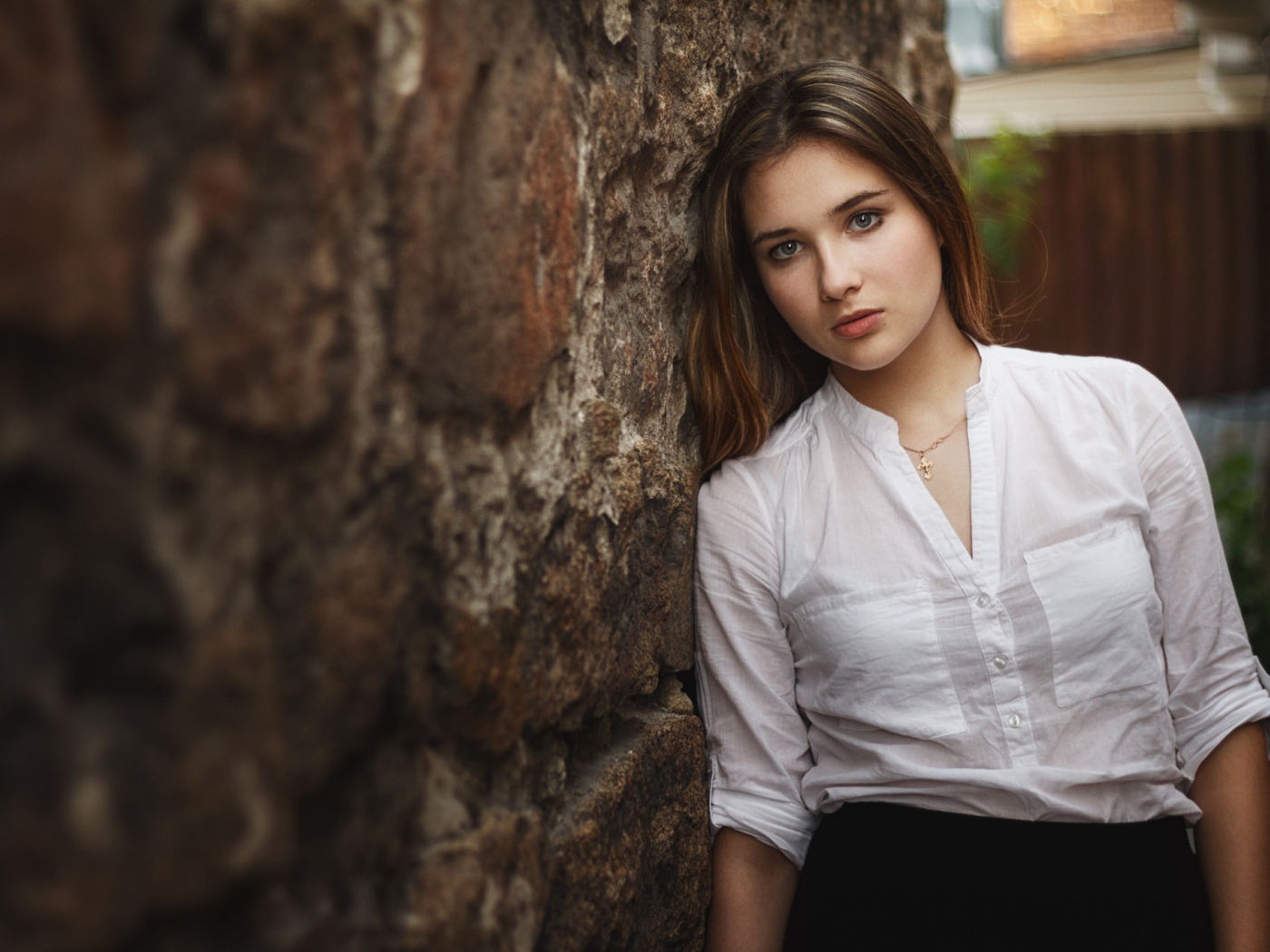 Девушка в белой рубашке стоит у стены