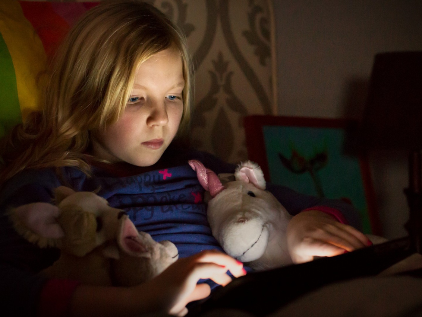 Девочка играет с планшетом лежа в кровати