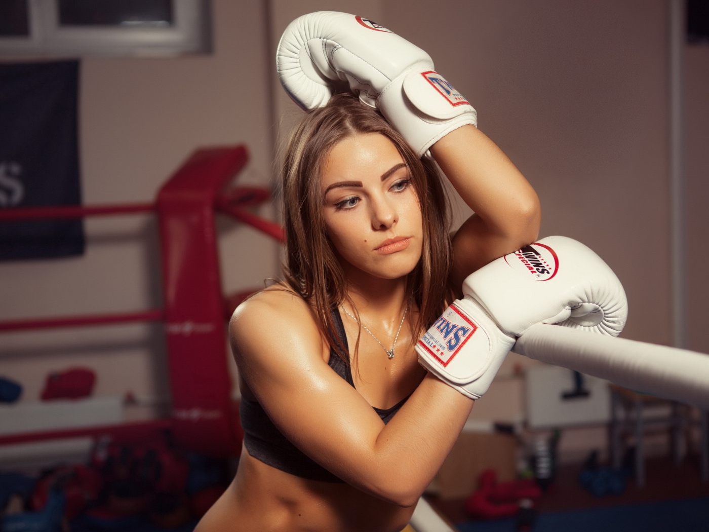 Девушка в белых перчатках отдыхает у канатов ринга