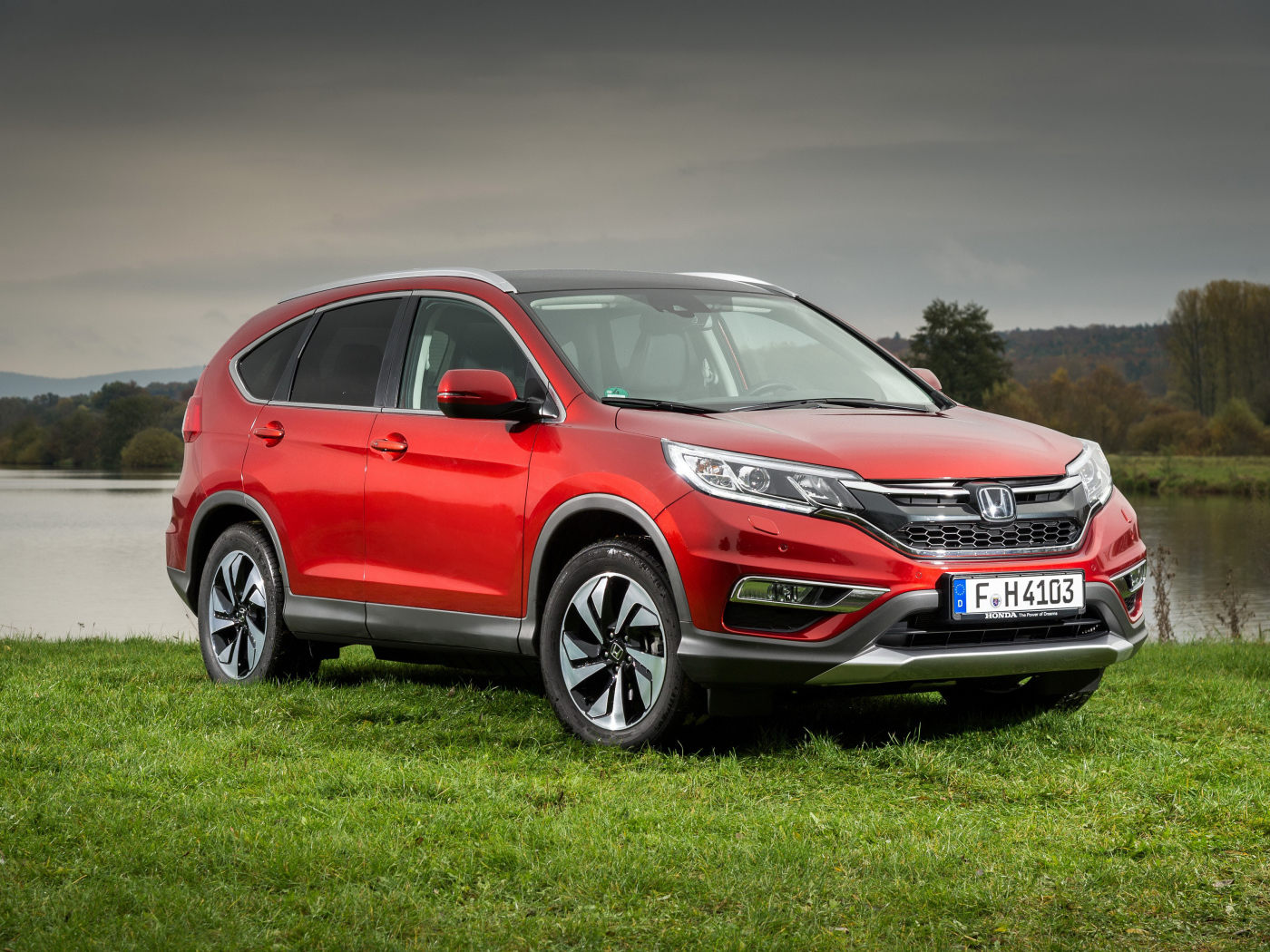 Красный внедорожник Honda CR-V стоит на зеленой траве у реки