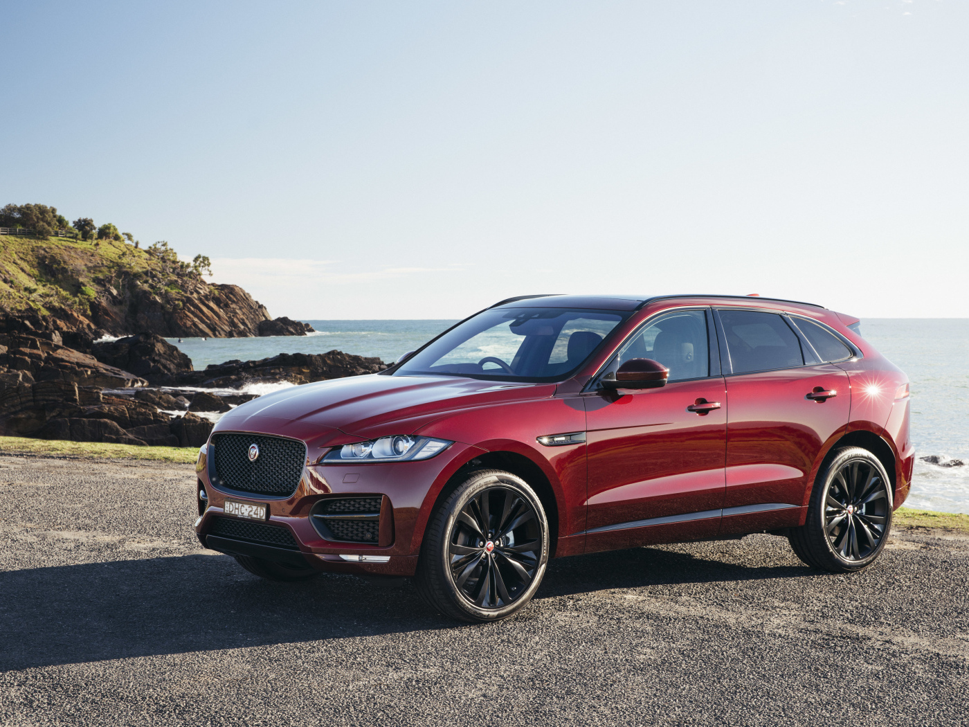 Бордовый автомобиль Jaguar F-Pace на фоне океана