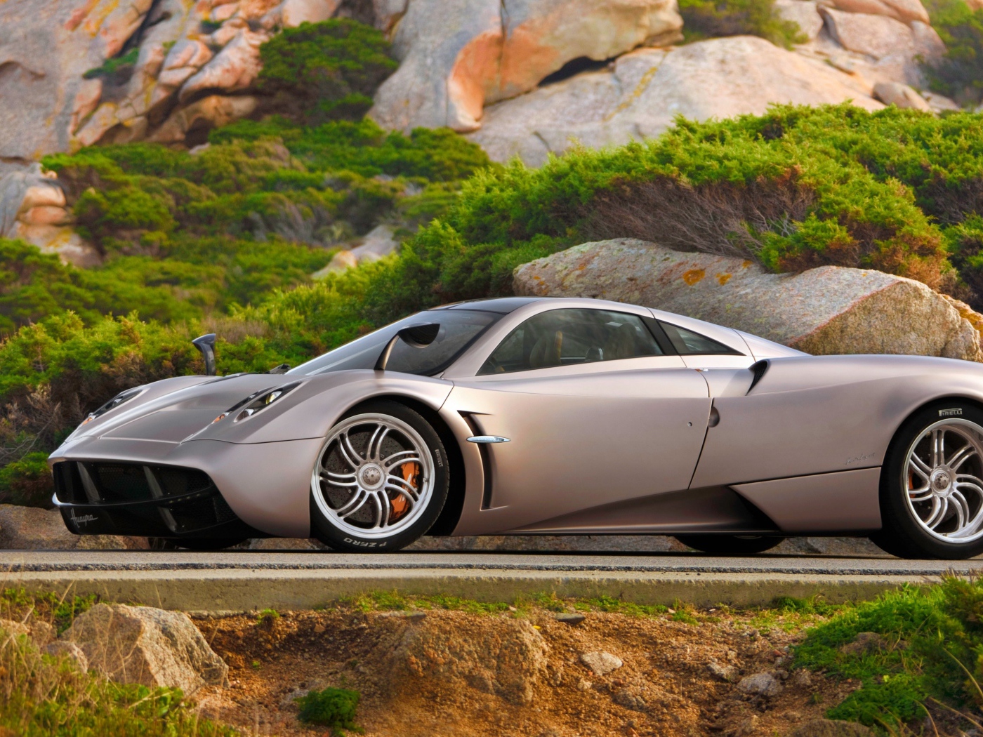 Серебристый быстрый автомобиль  Pagani Huayra на трассе у скалы