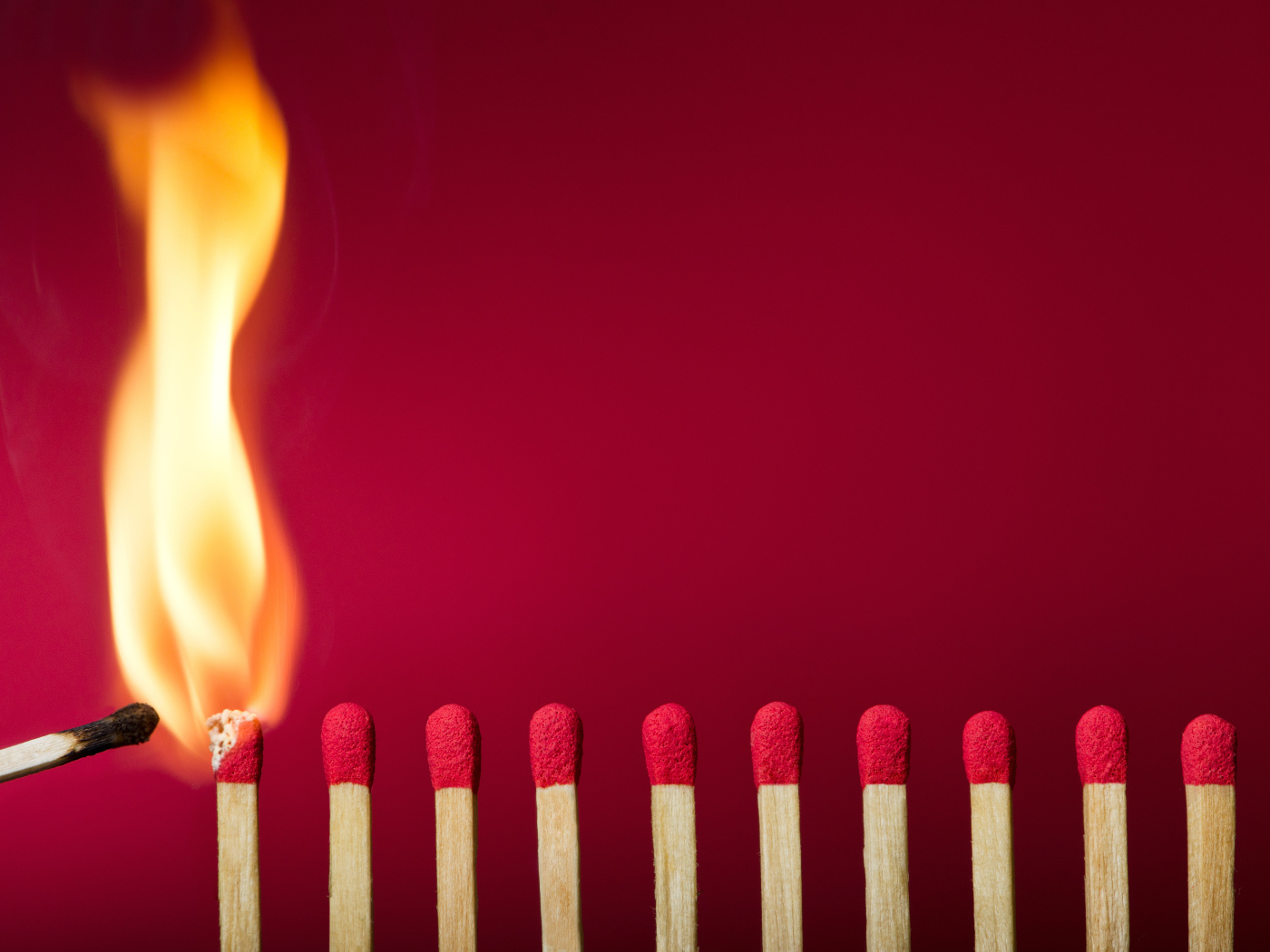 Зажженная спичка и спички на красном фоне