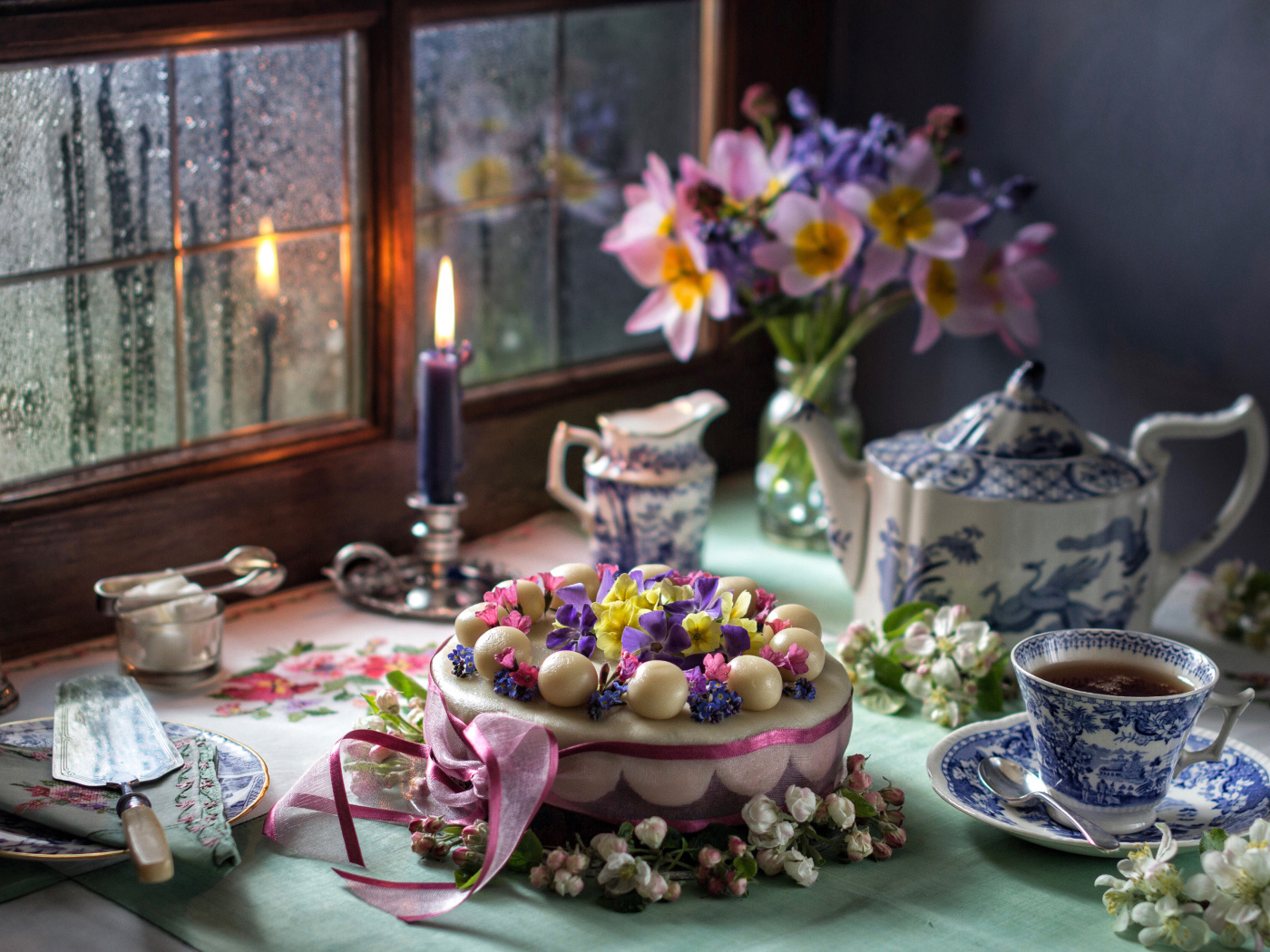 Красивый торт на столе с сервизом и горящей свечой у окна