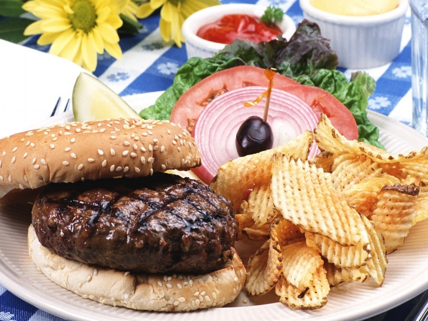 Гамбургер с котлетой и картофельные чипсы на тарелке с овощами