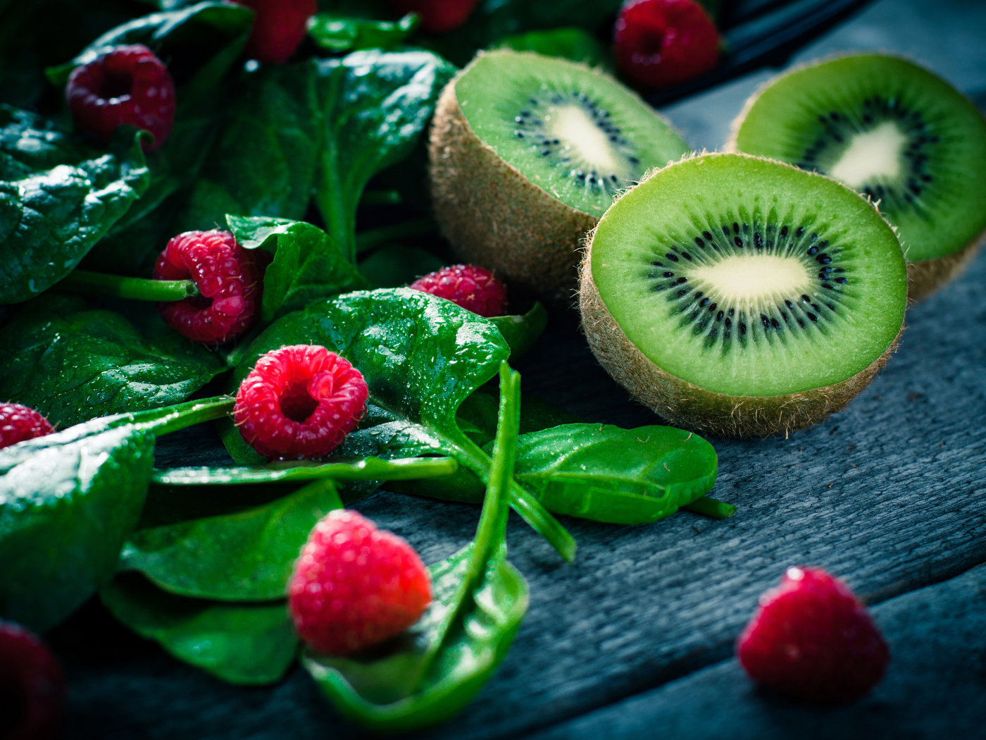 Половинки киви на столе с зелеными листьями и свежей малиной