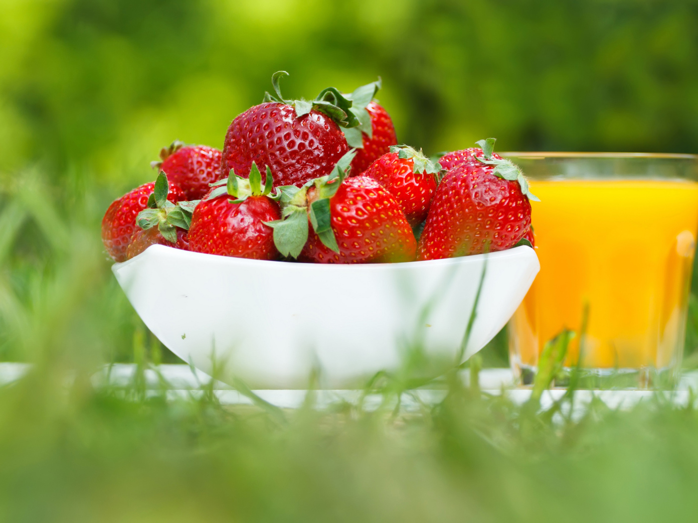 Спелые ягоды клубники и стакан апельсинового сока на зеленой траве