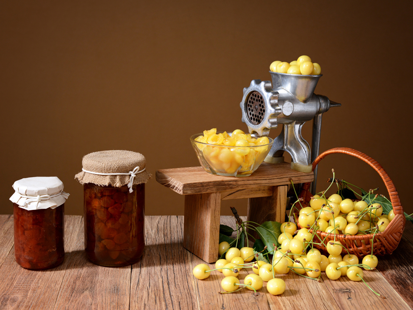 Две баночки варенья и желтые черешни на столе с мясорубкой