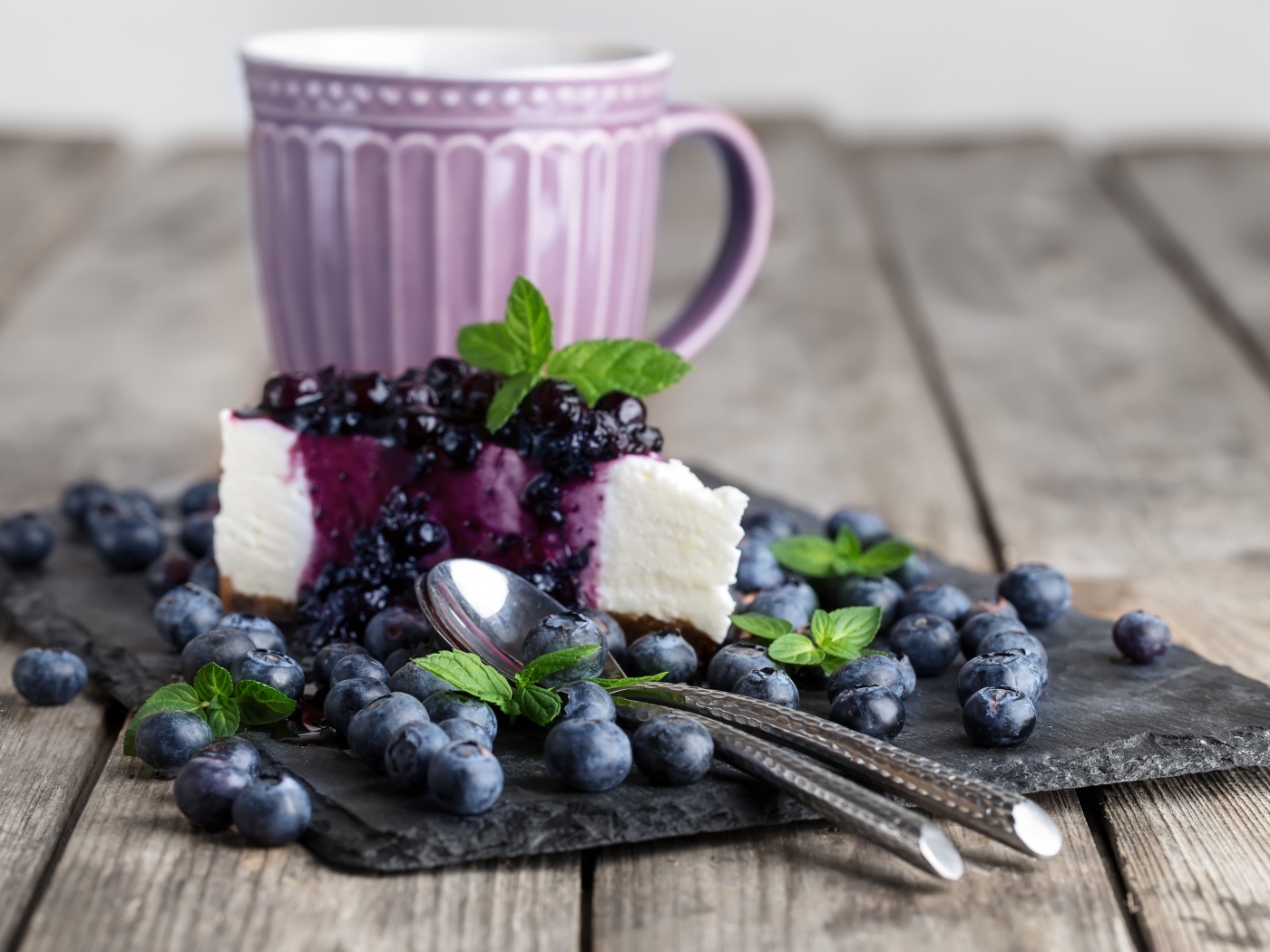 Черничный чизкейк со свежими ягодами лежит на столе с чашкой