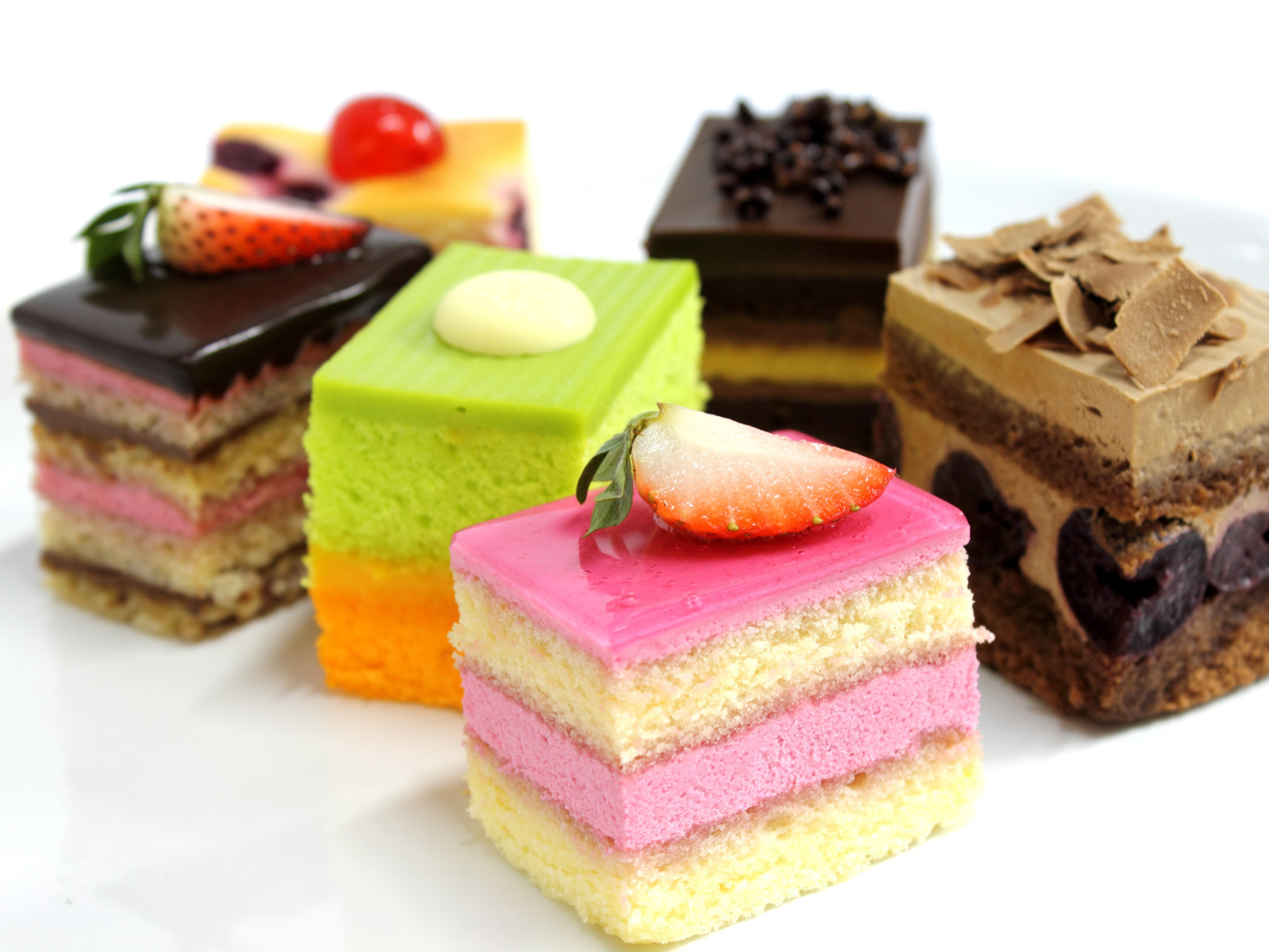 Разноцветные пирожные с ягодами на белом фоне