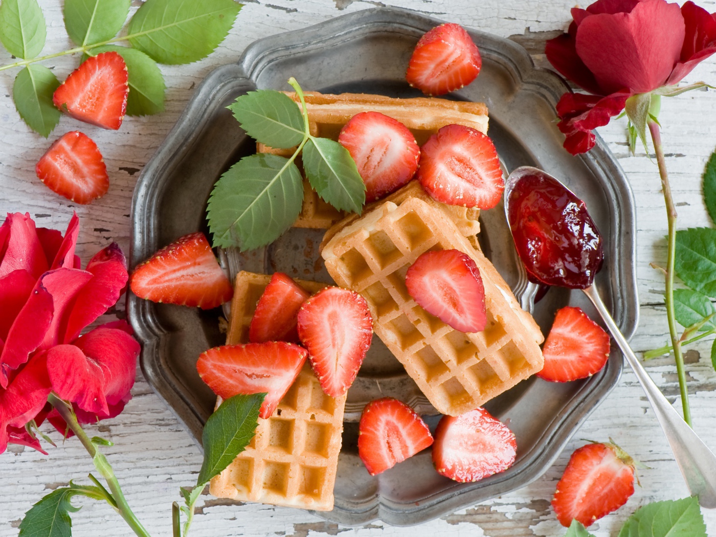 Сладкие вафли со свежей клубникой и красными розами на столе