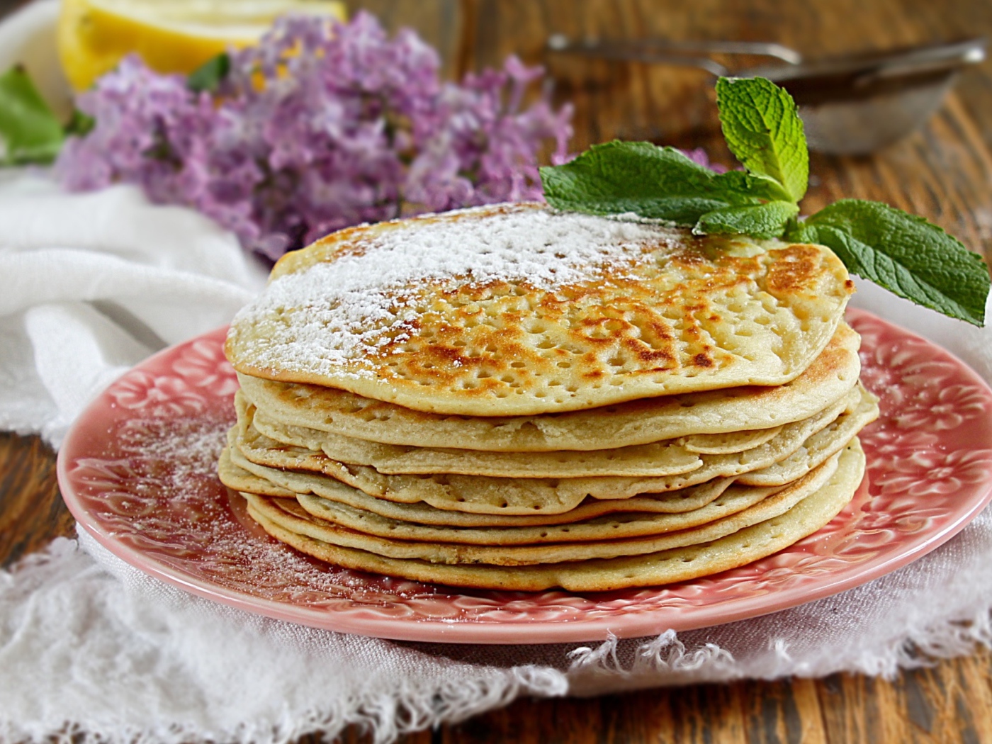 Тонкие блинчики на тарелке с сахарной пудрой и веточкой мяты