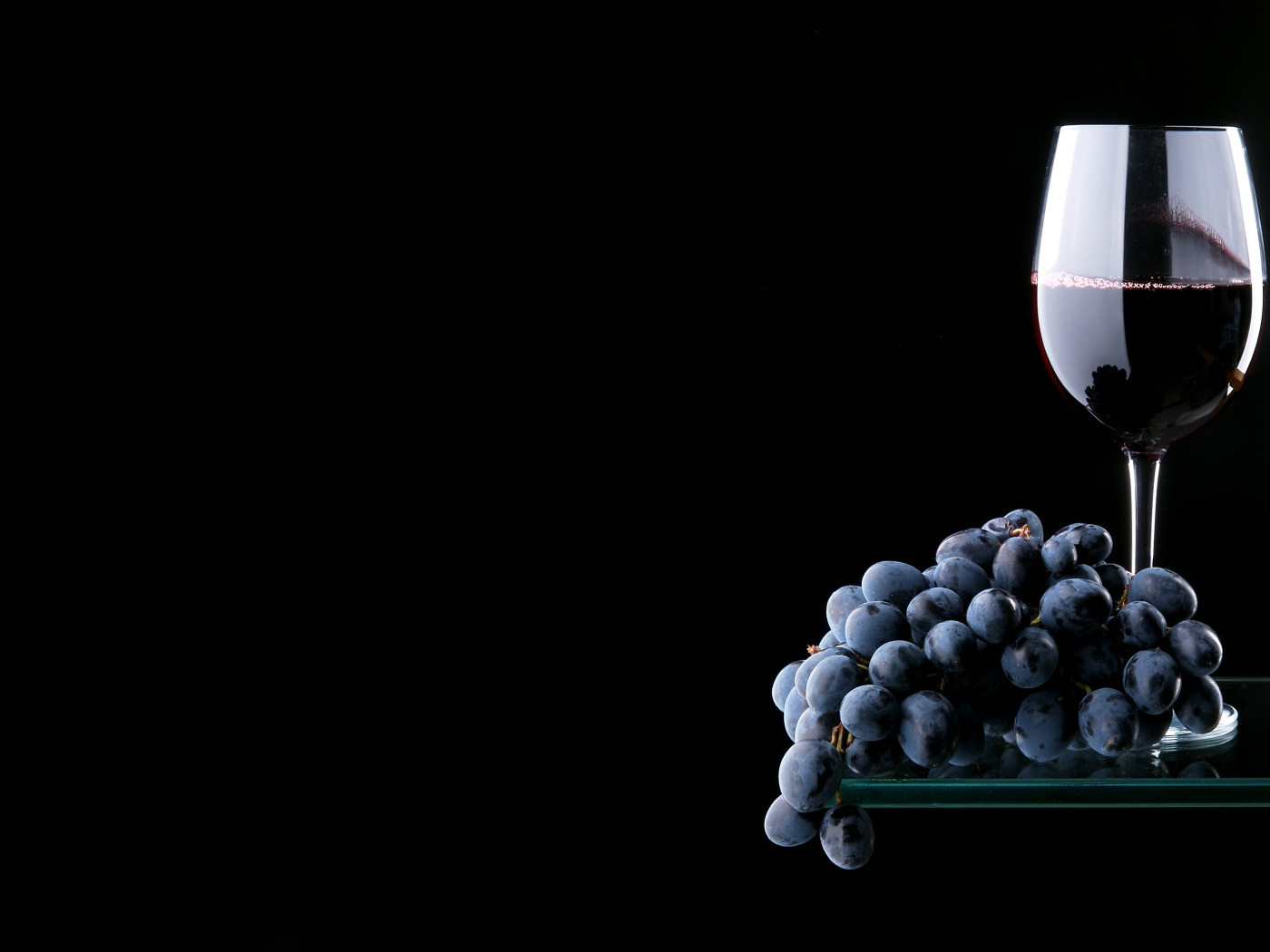 Гроздь синего винограда с бокалом красного вина на черном фоне