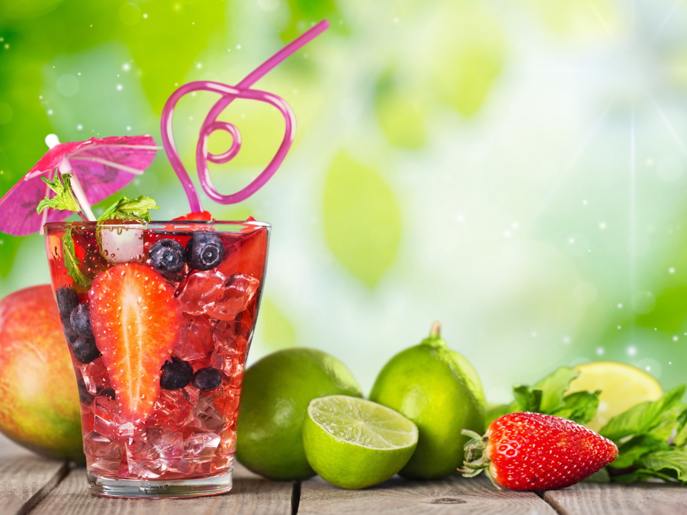 Коктейль с клубникой и ягодами черники в стакане со льдом на столе с лаймами и клубникой