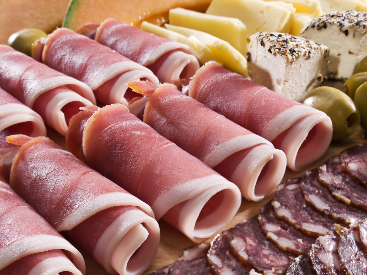 Аппетитные рулетики из бекона на тарелке с зелеными оливками