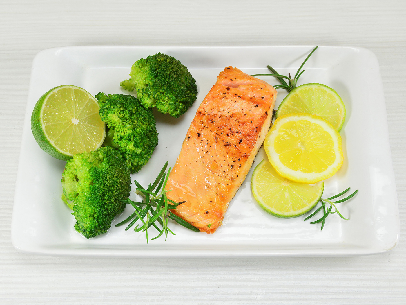 Красная рыба на белой тарелке с лимонами и брокколи
