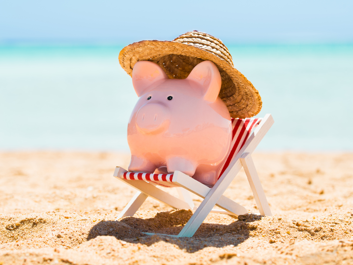 Сувенир свинка в шляпе лежит в игрушечном кресле на пляже