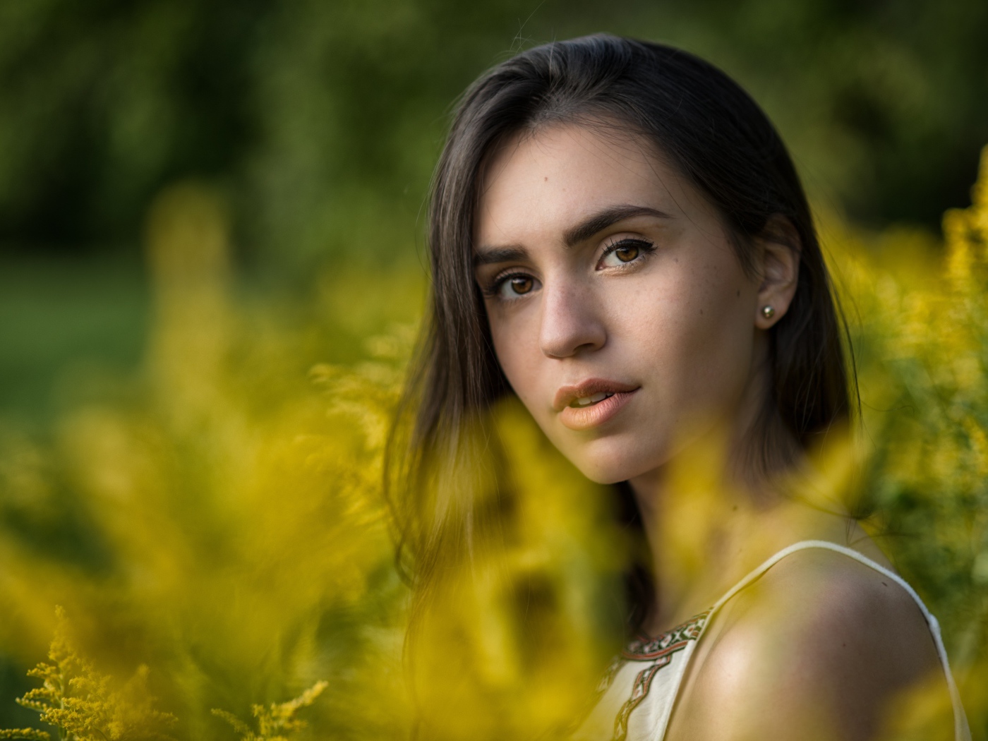 A beautiful girl with a tender gaze sits at the yellow flowers