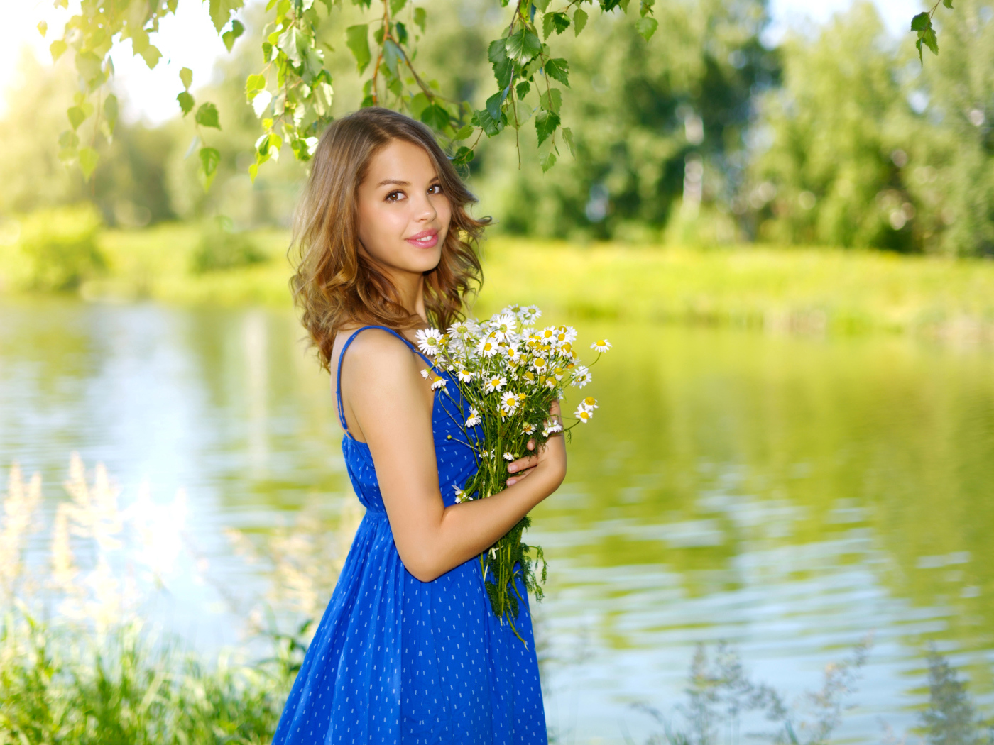 Красивая девушка шатенка в синем сарафане с букетом ромашек у воды