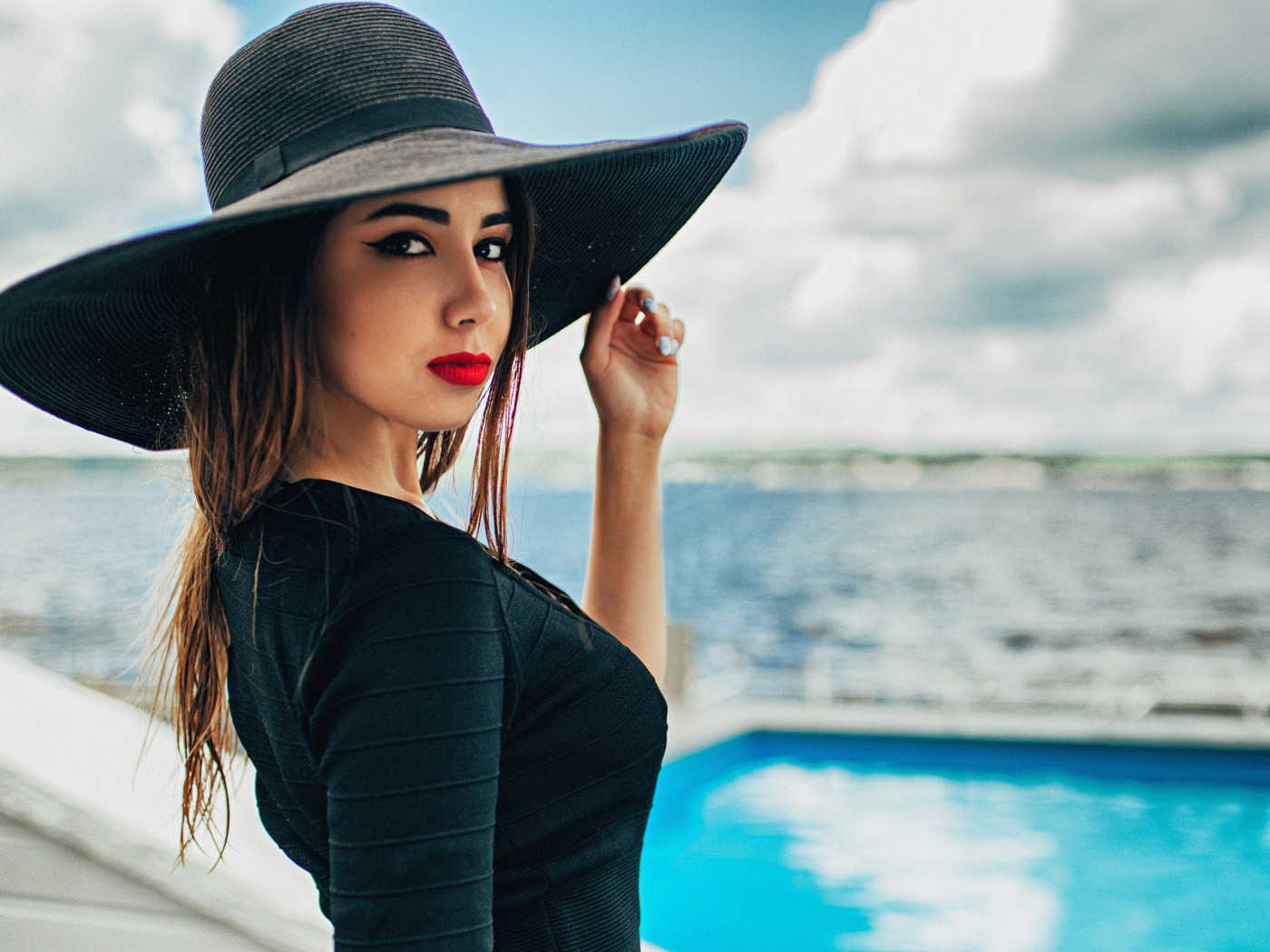 Красивая девушка в большой черной шляпе у бассейна