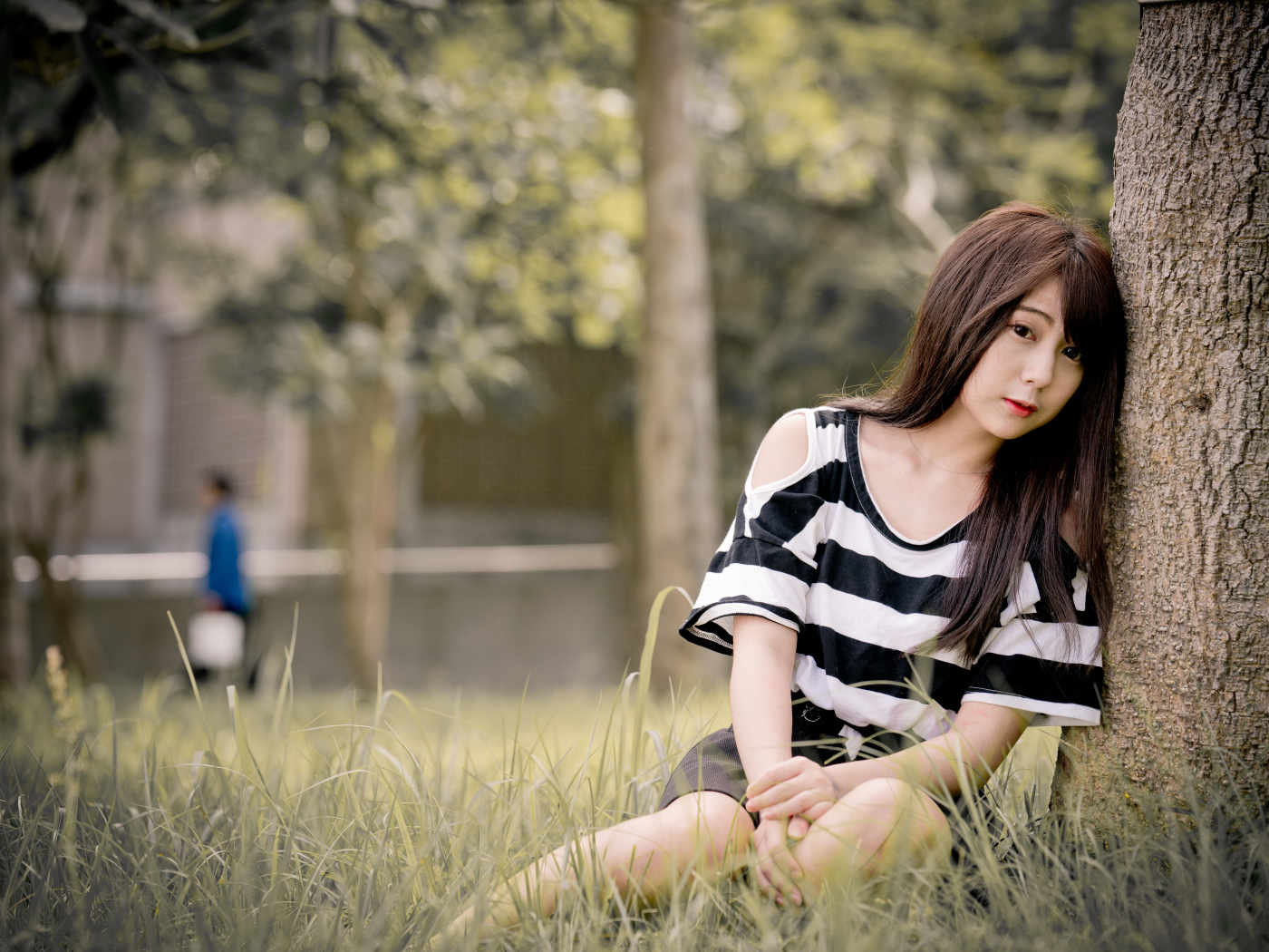 Молодая девушка азиатка сидит на траве у дерева