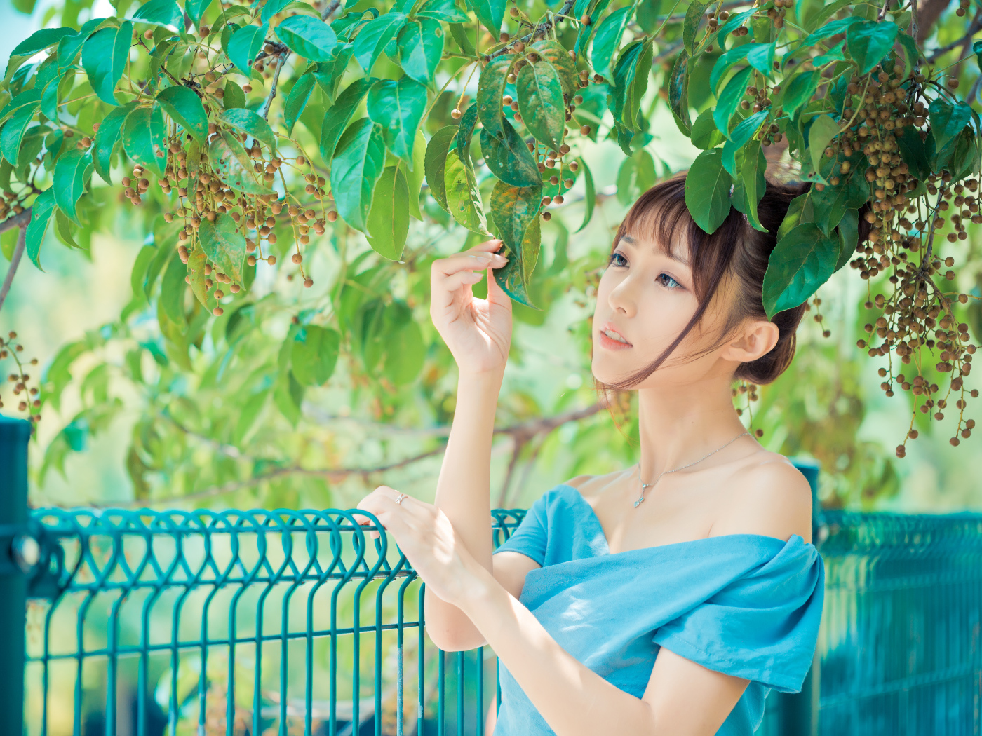 Молодая красивая девушка азиатка стоит у ветки с зелеными листьями