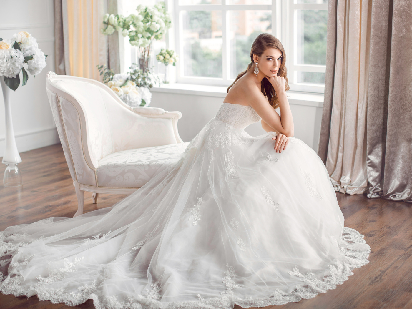 Молодая девушка в красивом свадебном платье сидит в белом кресле