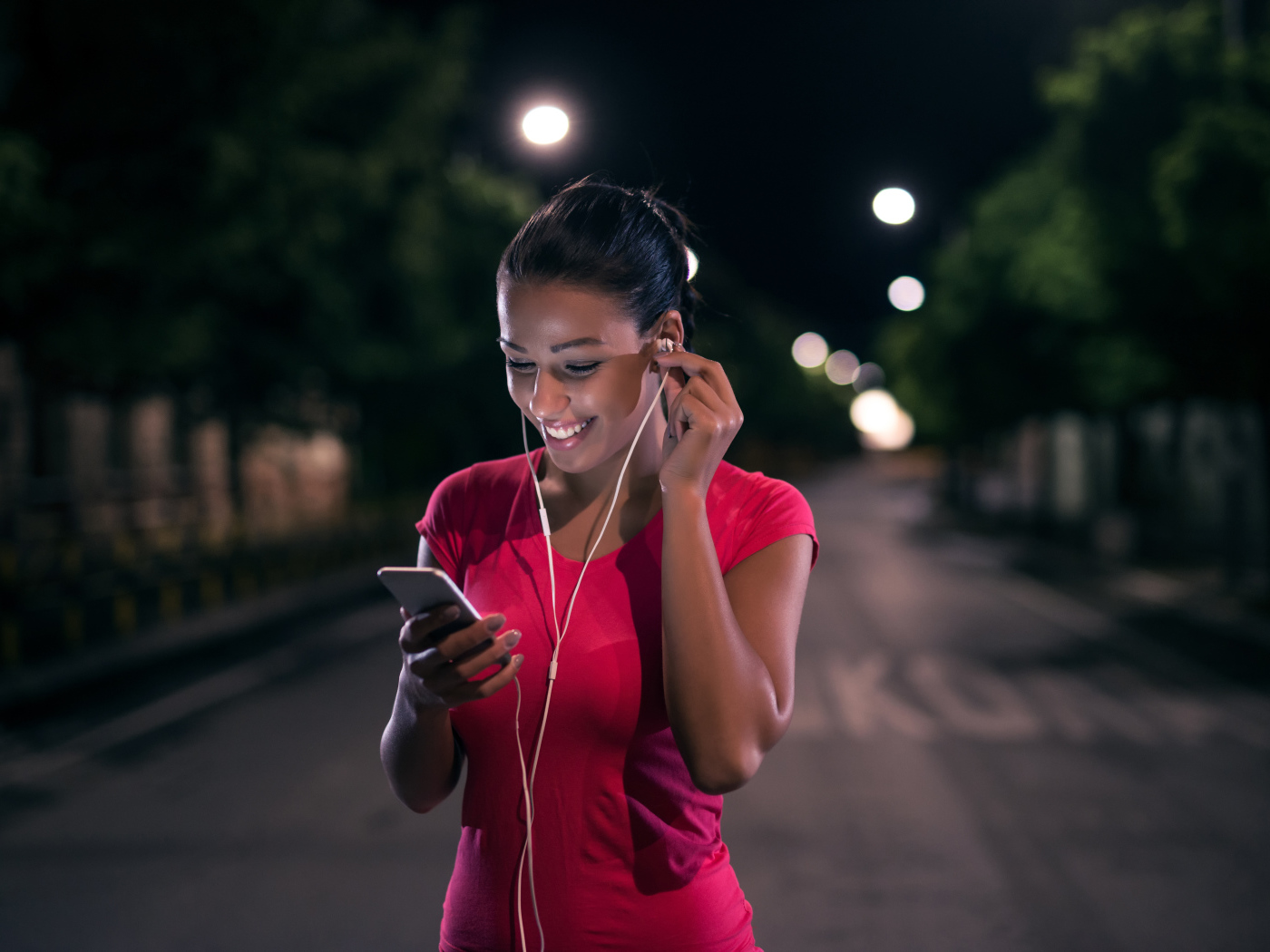 Молодая улыбающаяся девушка в наушниках с телефоном в руках