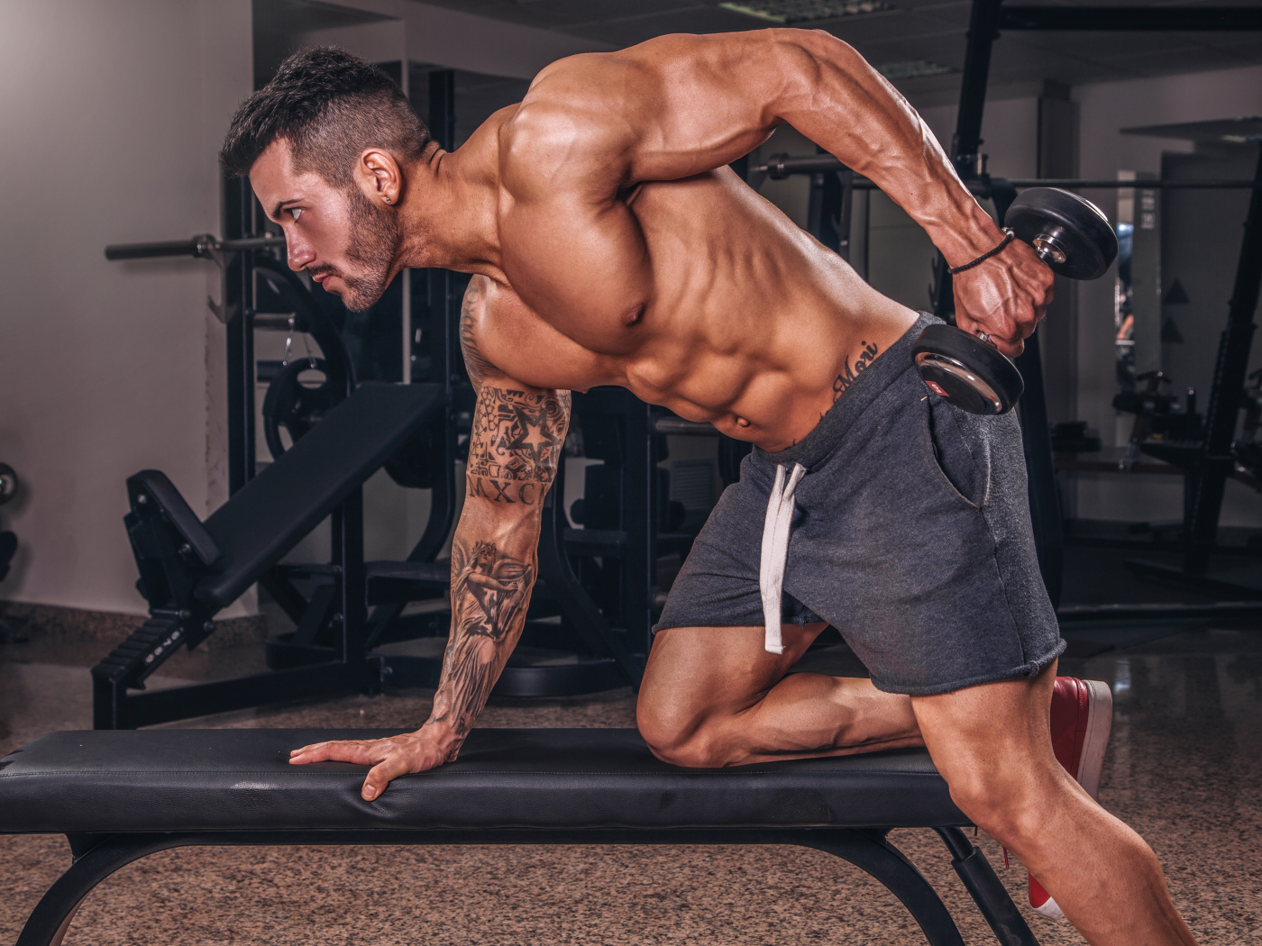 Мускулистый мужчина занимается в спортзале с гантелей