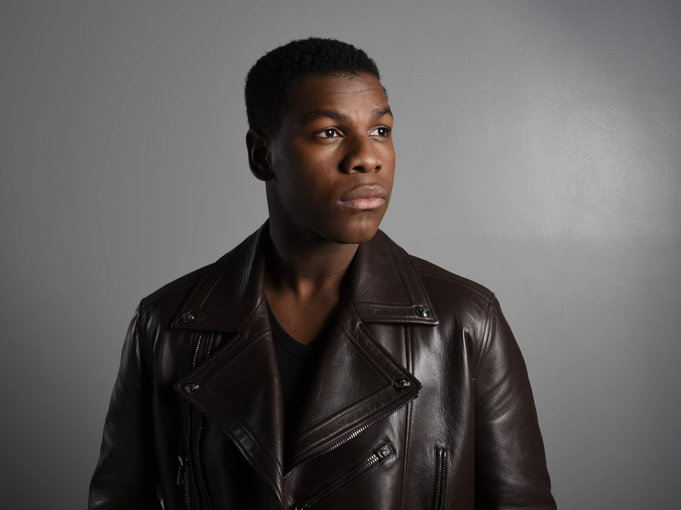 Актер  Джон Бойега в кожаной куртке на сером фоне