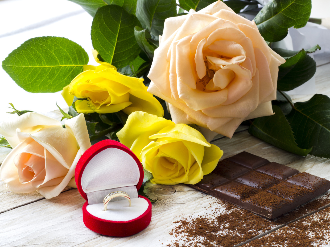 Букет роз на столе с шоколадкой и красной коробочкой с обручальным кольцом