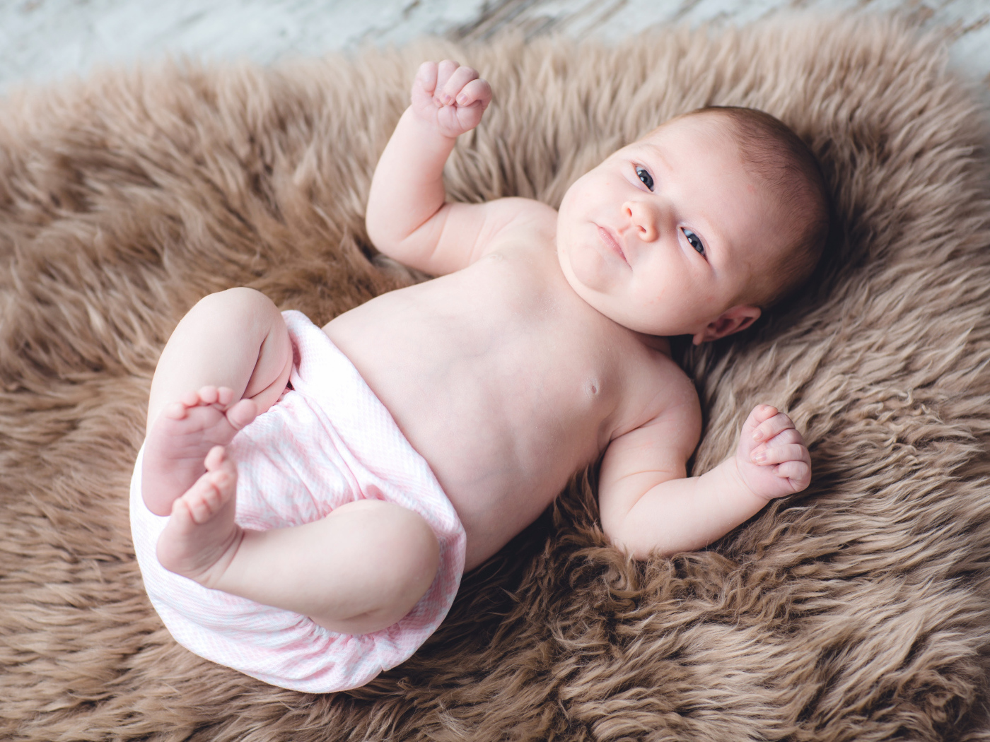 Грудной ребенок лежит на меховом покрывале