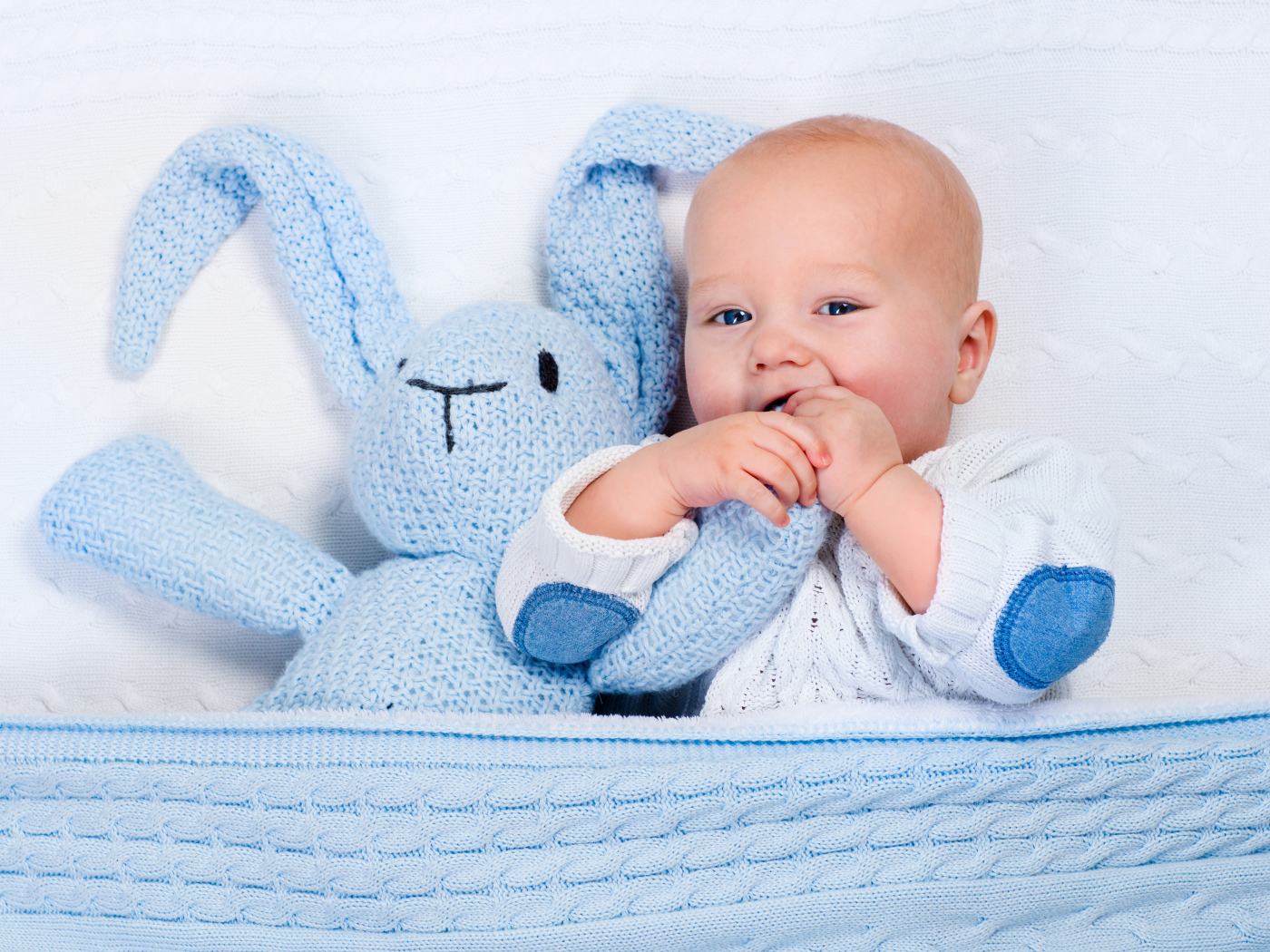 Милый младенец лежит в кроватке с голубым вязаным зайцем