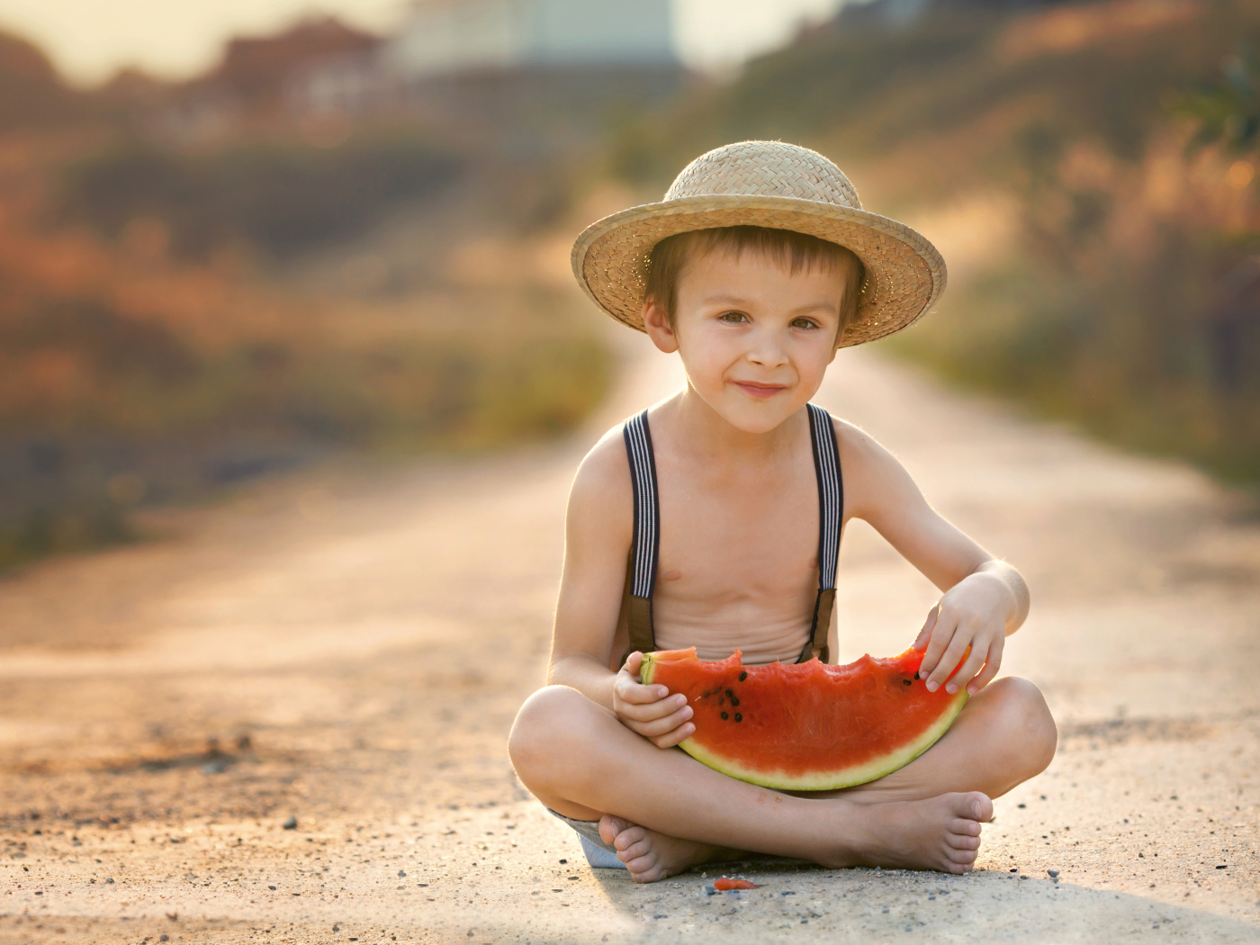 Маленький мальчик в шляпе сидит на дороге с долькой арбуза