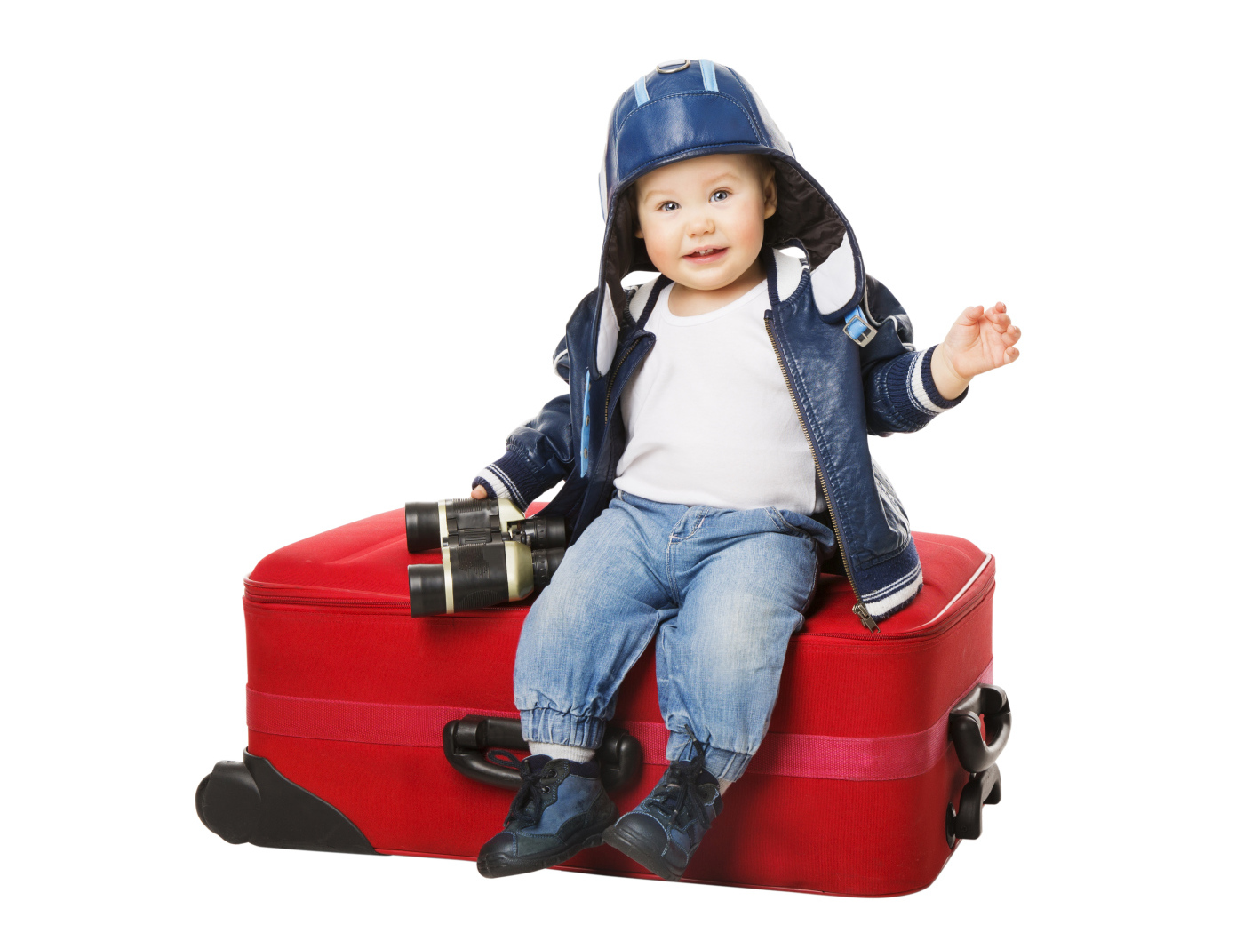 Маленький мальчик в шапке с биноклем сидит на красном чемодане