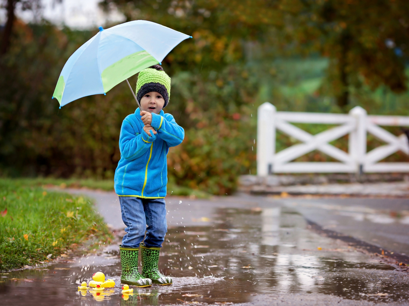 Маленький мальчик под зонтом гуляет по лужам